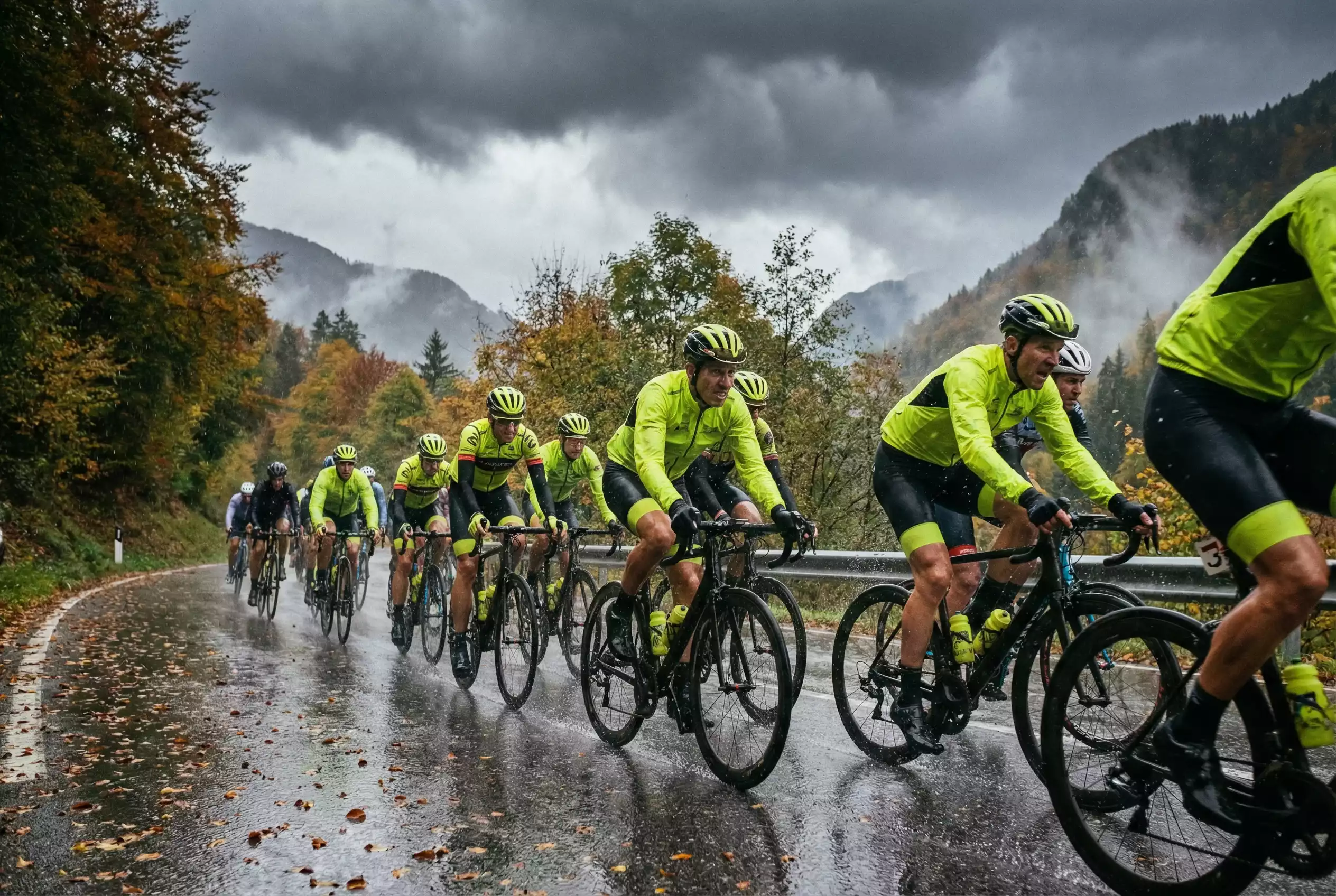 Gruppo di ciclisti professionisti in gara sotto la pioggia su strada bagnata con nuvole scure
