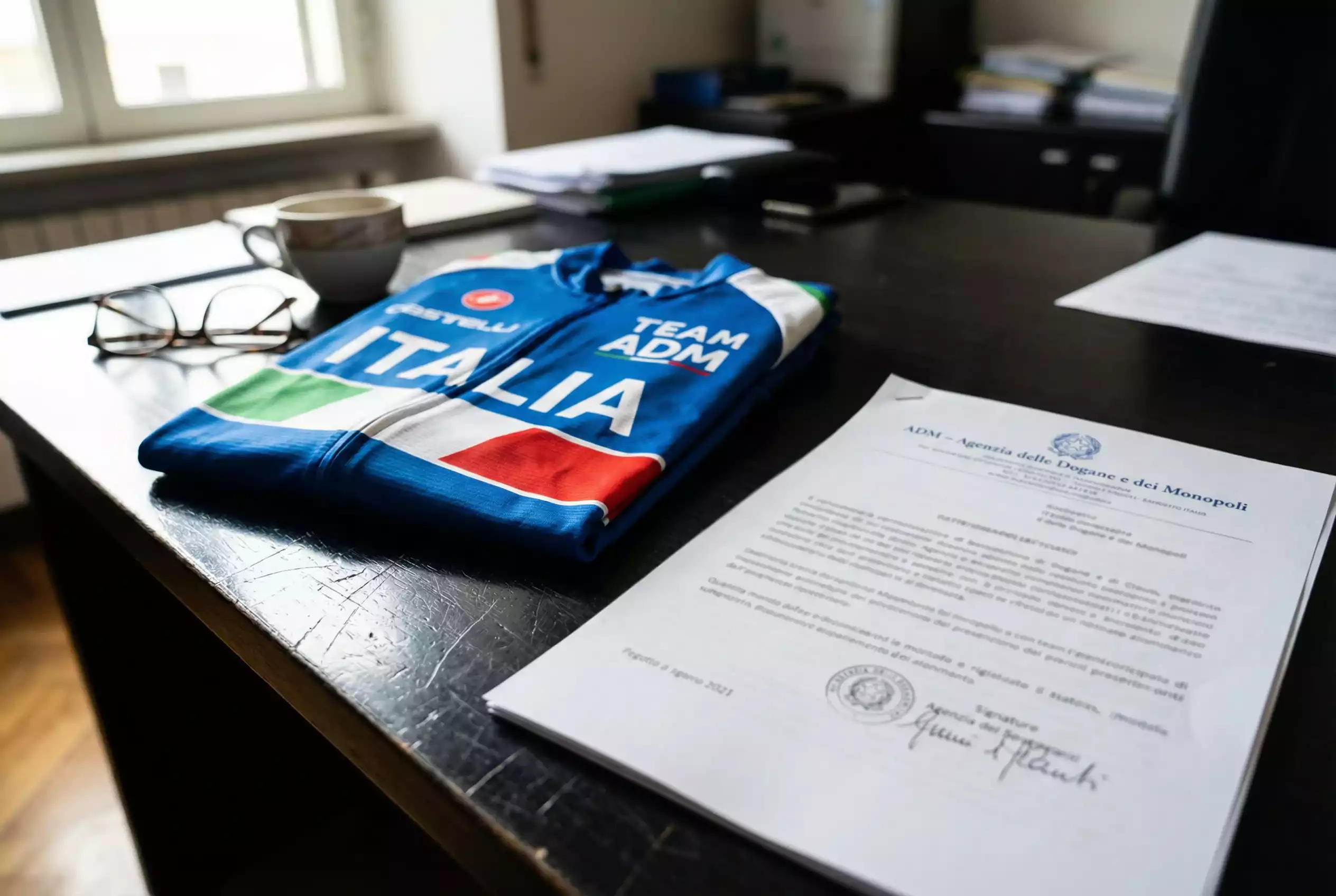 Documento normativo con simboli del ciclismo professionistico e bandiera italiana su scrivania istituzionale