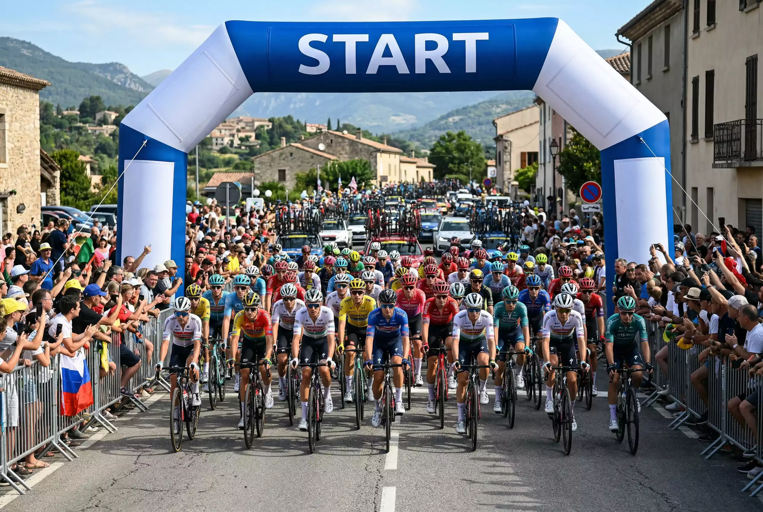 Gruppo di ciclisti alla partenza di una grande corsa a tappe con striscione di partenza visibile