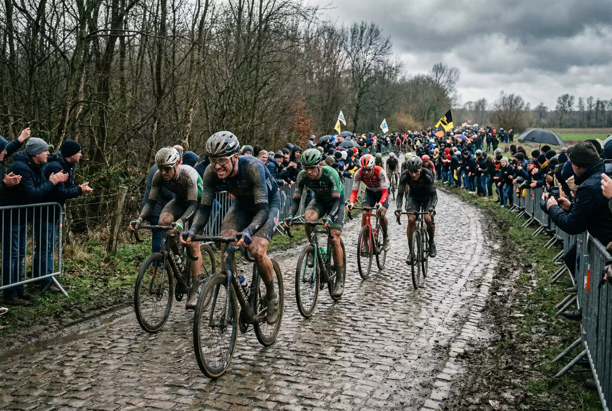 Ciclisti professionisti in gruppo compatto su un tratto di pavé durante una classica del nord