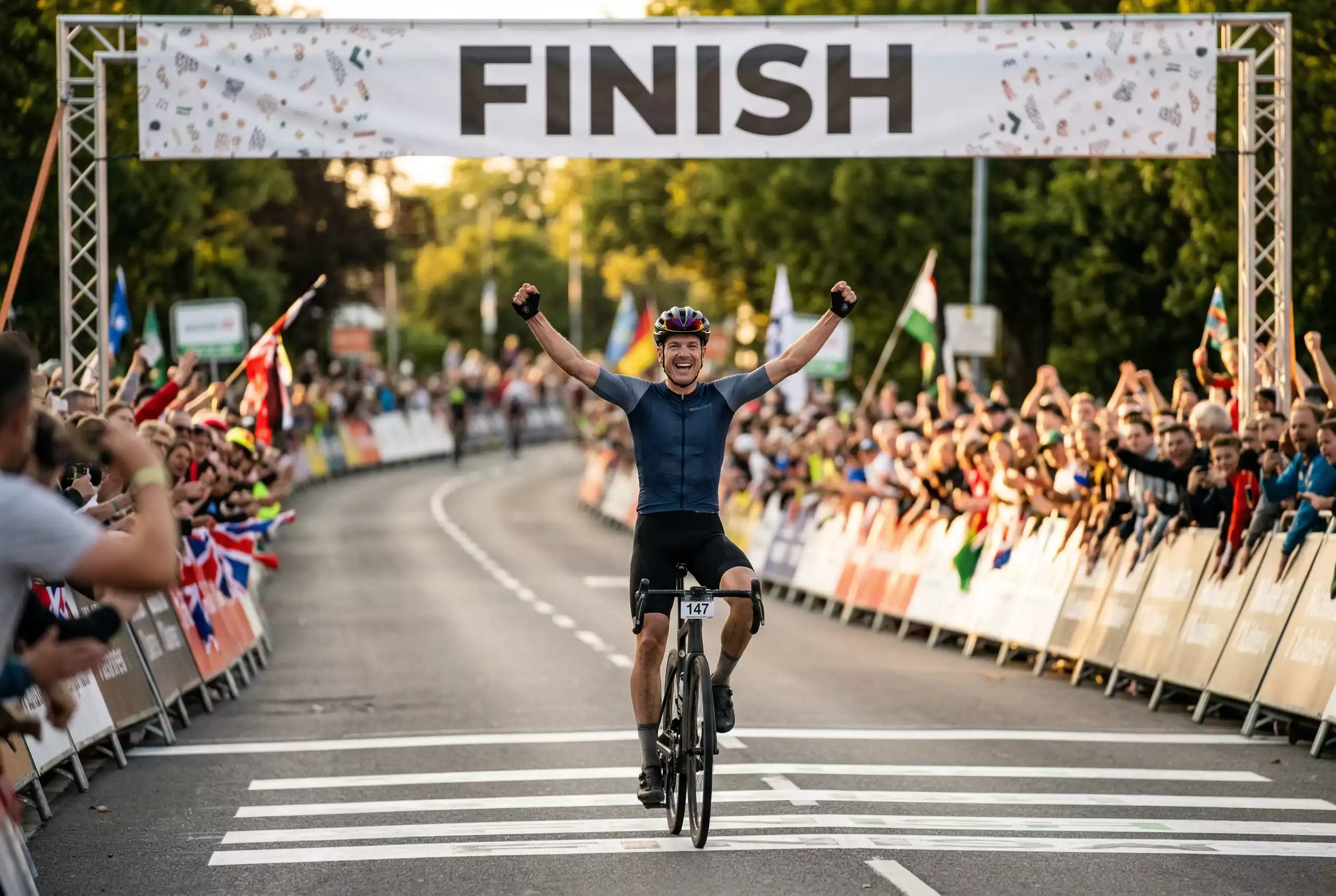 Ciclista professionista che taglia il traguardo di tappa con le braccia alzate in segno di vittoria